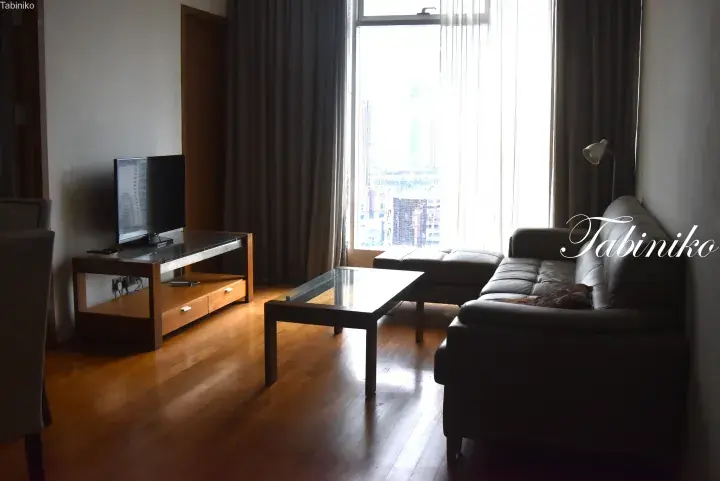 Modern living room with wooden floors, leather sofa, and city view from high-rise apartment window