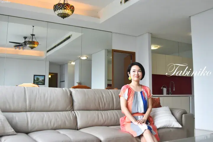 Woman sitting on a beige leather sofa in a modern apartment living room with mirrored walls and a stained glass ceiling light.