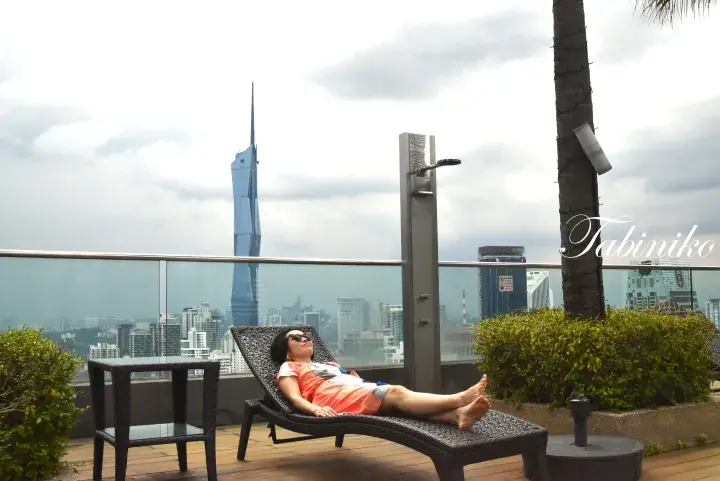Woman relaxing on a rooftop lounge chair with a view of the Merdeka 118 tower in Kuala Lumpur.