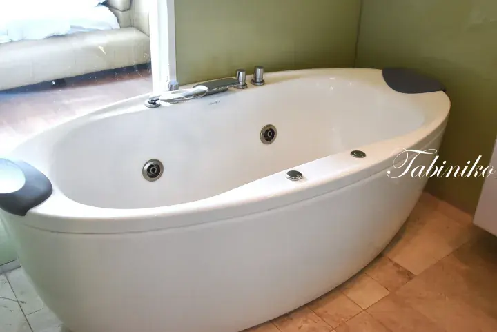 Modern white freestanding jacuzzi bathtub with chrome fixtures in a hotel bathroom.