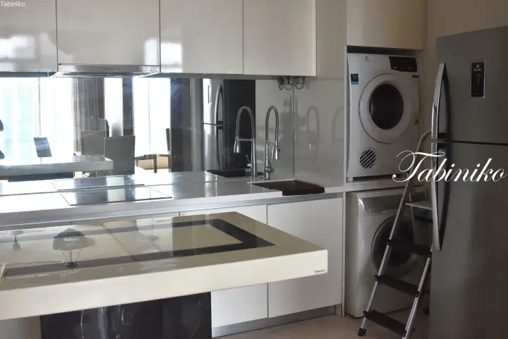 Modern kitchen with white glossy cabinets, stainless steel appliances, and a stacked washer and dryer.