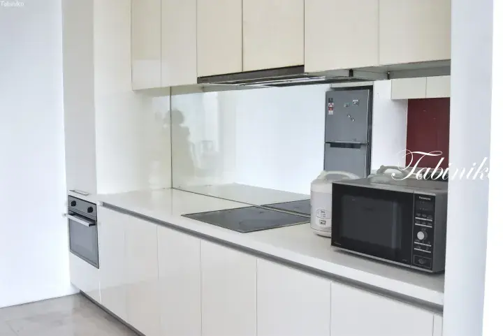 Modern white kitchen with built-in oven, induction cooktop, microwave, and refrigerator in a Malaysian property.