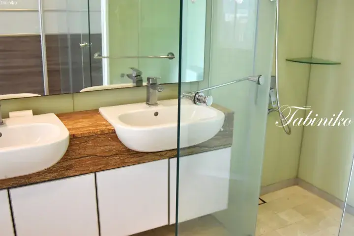 Modern bathroom with dual white sinks on a brown marble countertop and a glass shower enclosure.