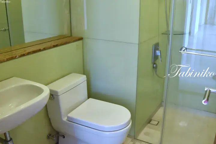 Modern bathroom with light green tiles, white sink, toilet, and glass shower enclosure.