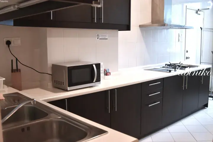 Modern kitchen with dark cabinets, white countertops, microwave, and gas stove in a serviced residence.