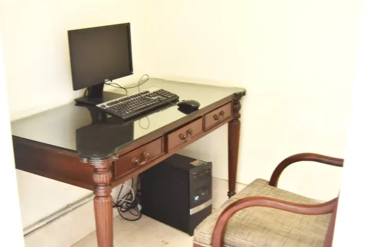 A wooden desk with a glass top, computer monitor, keyboard, and tower, set up for work in a property.
