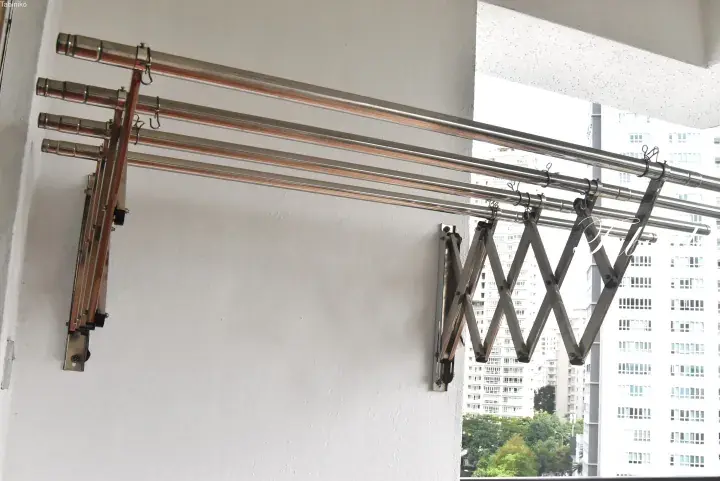 Stainless steel retractable clothes drying rack mounted on a balcony wall with high-rise buildings in the background.