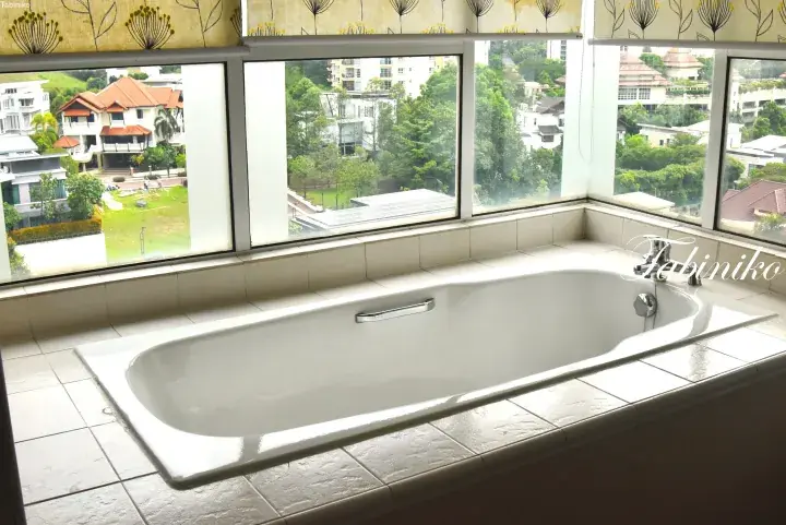 White built-in bathtub with a large window overlooking lush greenery and residential villas in a Malaysian property.