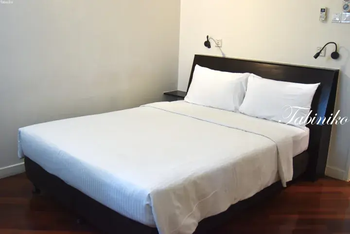 Neatly made double bed with white linens and dark wood headboard in a modern hotel room.