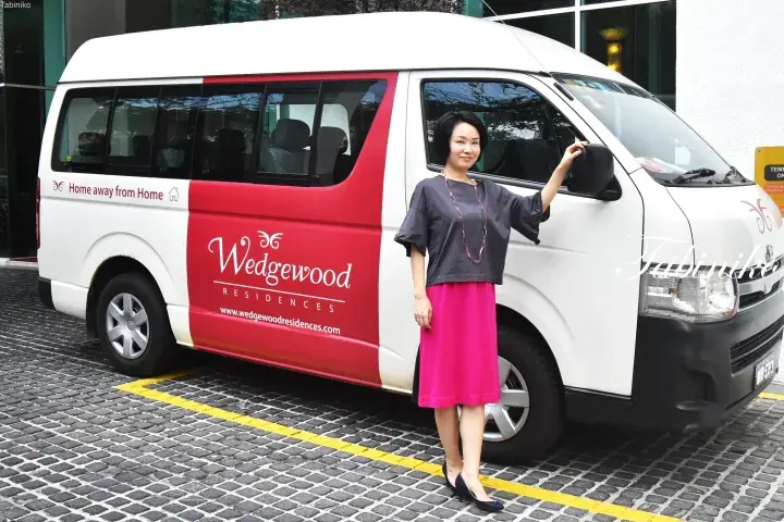 Woman standing beside a Wedgewood Residences shuttle van parked on a paved driveway.