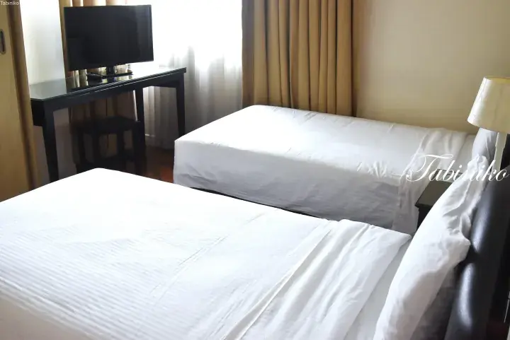 Twin beds with white linens in a hotel room featuring a TV desk and curtains.