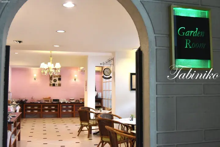 View into a bright dining area with a buffet setup, wicker chairs, and a sign reading ‘Garden Room’.