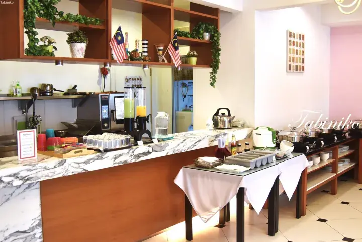 Buffet breakfast station with juice dispensers, egg corner, and Malaysian flags at a Malaysia hotel.