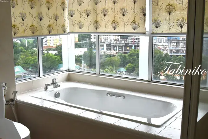 White bathtub in a bathroom with large windows overlooking a city view and construction site in Malaysia.