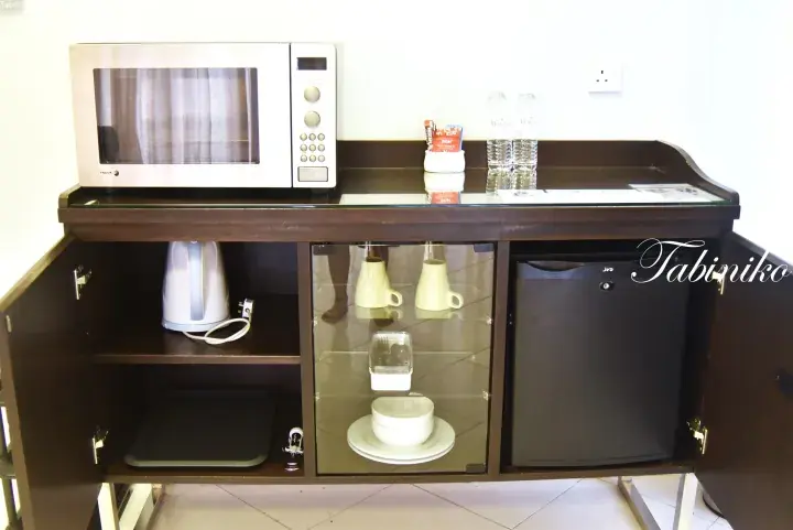 Hotel room kitchenette featuring a microwave, electric kettle, mini fridge, and complimentary tea and water.