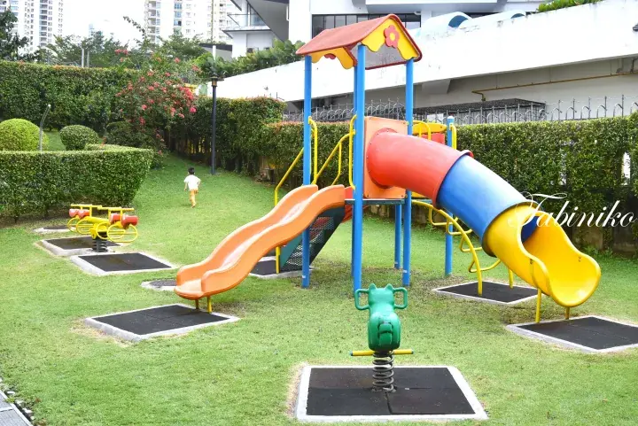 Colorful playground with slides and spring riders on a grassy lawn at a residential complex in Malaysia.