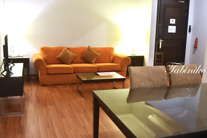 Bright living room with an orange sofa, glass coffee table, and wooden flooring in a modern Malaysian apartment.