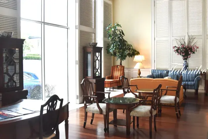 Bright living room with wooden floors, antique furniture, and large windows overlooking a street.