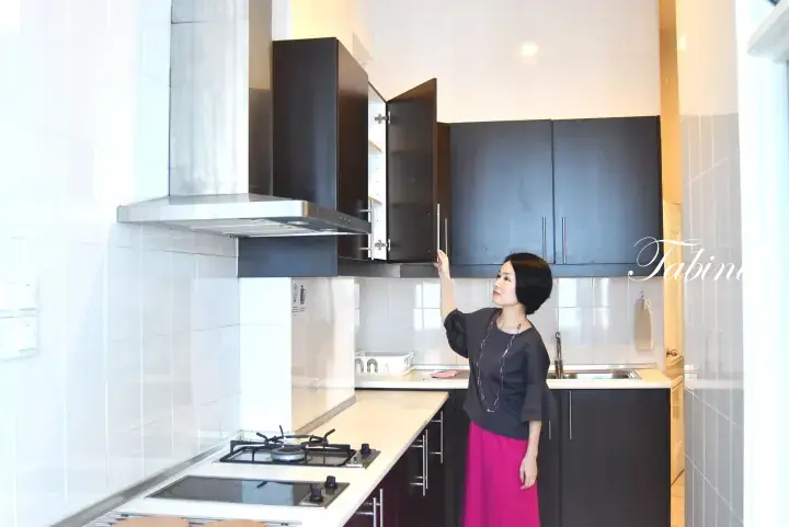 Woman in a modern kitchen opening a dark brown upper cabinet above a stainless steel range hood and gas stove.