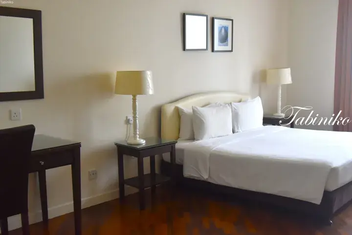 Spacious hotel room with a double bed, wooden flooring, and a desk area.