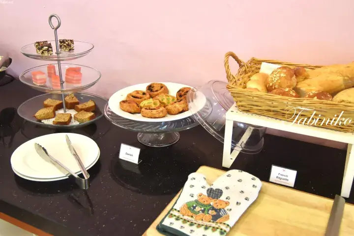 Buffet table displaying Danish pastries, French baguettes, and assorted cakes on tiered stands.