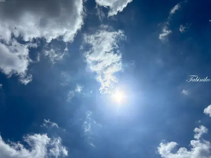 Bright sun shining through white clouds in a deep blue sky, evoking Malaysia&rsquo;s tropical weather.
