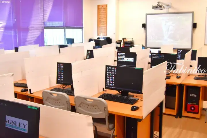 Computer lab with partitioned desks, monitors, and a projector screen at Kingsley National School in Malaysia.