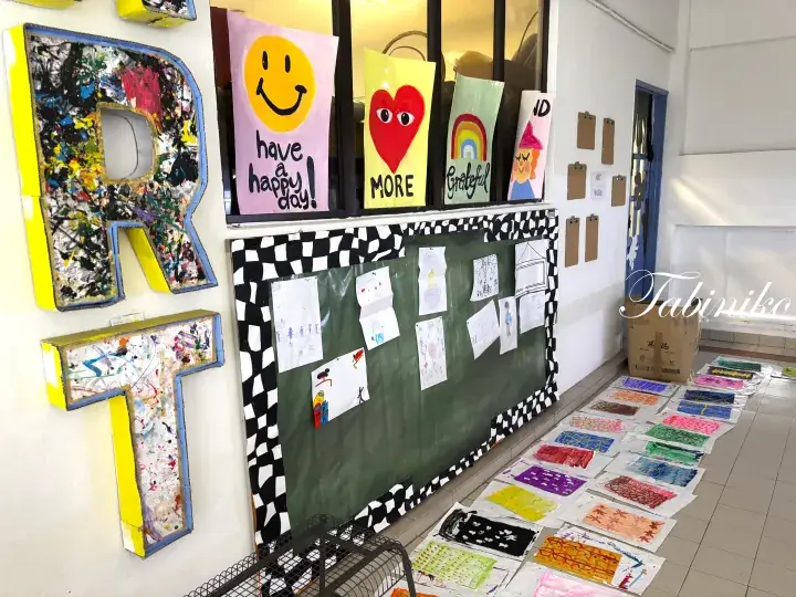Colorful children&rsquo;s artwork displayed on a wall and floor in a bright hallway, featuring large letters and cheerful drawings.