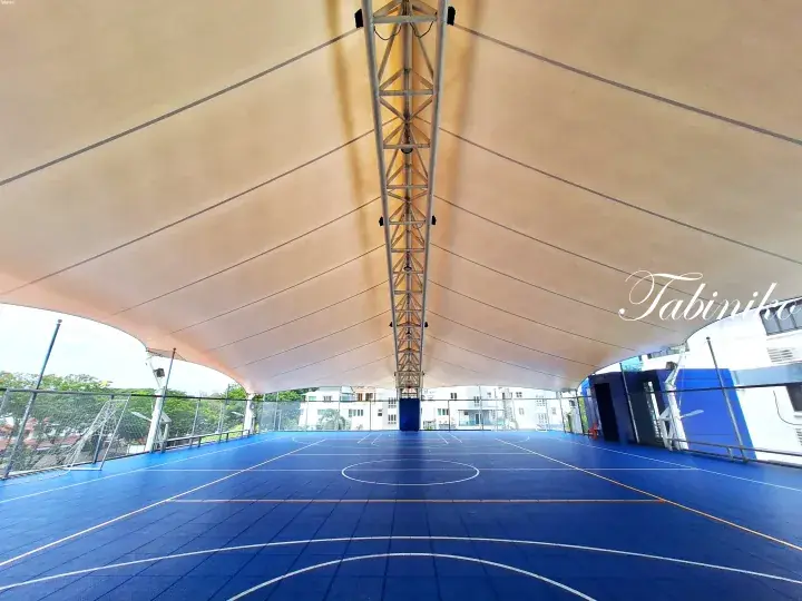 Blue basketball court under a large beige tensile fabric roof with a central metal truss at a Malaysia property.