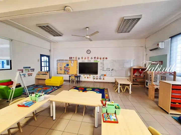 Bright preschool classroom with wooden tables, colorful rugs, and educational displays in a modern learning space.
