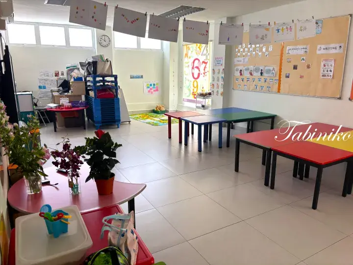 Bright preschool classroom with colorful tables, student artwork, and educational displays.