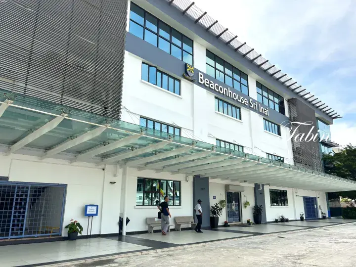 Modern white facade of Beaconhouse Sri Inai school building with glass canopy entrance and security guard.