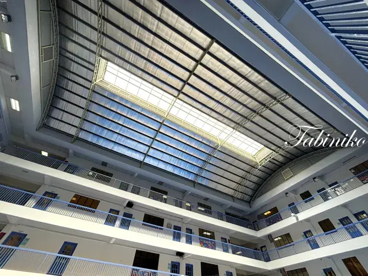 Interior view of a multi-story atrium with blue railings and a large skylight ceiling.