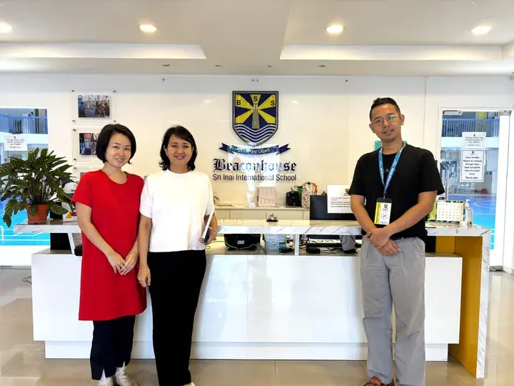 Three people standing at the reception desk of Beaconhouse Sri Inai International School in Malaysia.