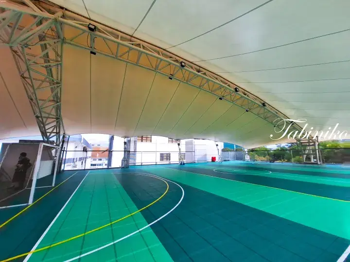 Spacious covered sports court with green flooring and white tensile roof structure at a modern property.