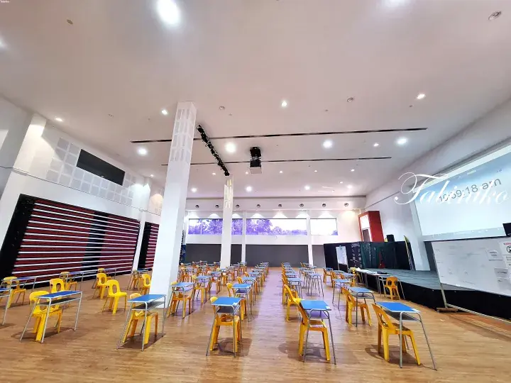 Bright event hall with yellow chairs, blue desks, and a stage, ready for a presentation or workshop.
