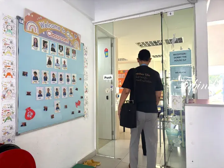 Man entering a classroom with a welcome sign and student photos displayed on the wall.