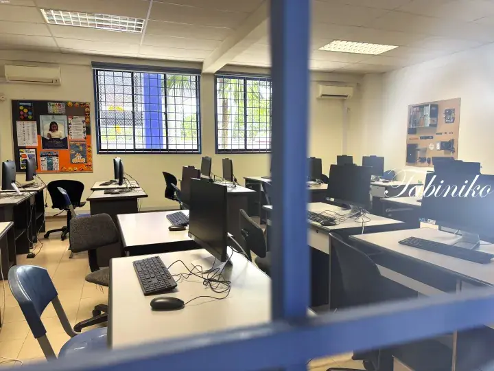 Modern computer lab with rows of desktops, ergonomic chairs, and educational posters on the walls.