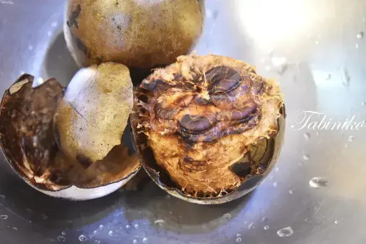 Close-up of a roasted durian fruit with its shell cracked open, revealing the brown, fibrous flesh inside.