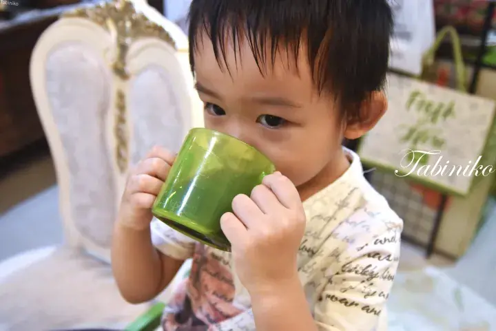 緑色のマグカップを両手で持ち、カフェで飲む幼い子供。
