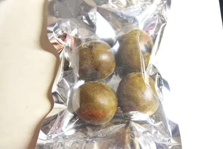 真空パックされた透明な袋に入った、丸い茶緑色の果物4個。