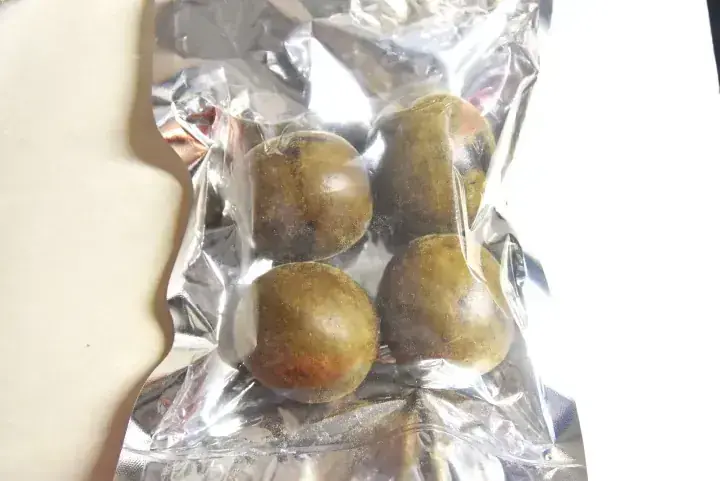 Four round, brownish-green fruits sealed in a clear vacuum-packed plastic bag.