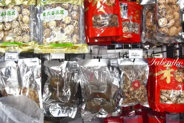Shelves stocked with various dried mushrooms and ingredients in colorful packaging at a Malaysian grocery store.