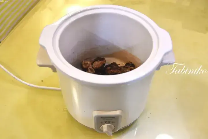 White Panasonic slow cooker containing dried ingredients on a yellow countertop.