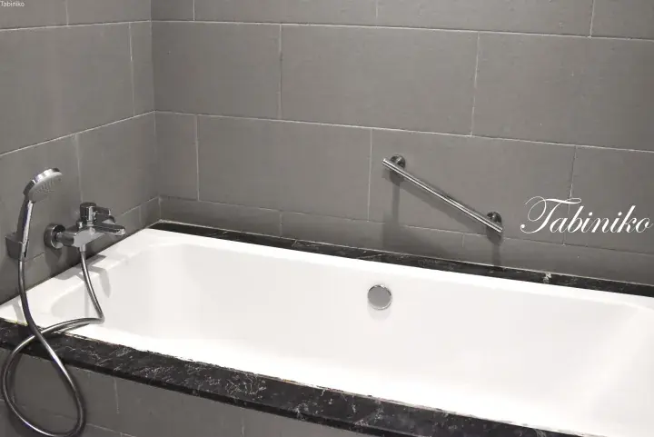 Modern white bathtub with grey tiled walls and a chrome grab bar in a stylish bathroom.