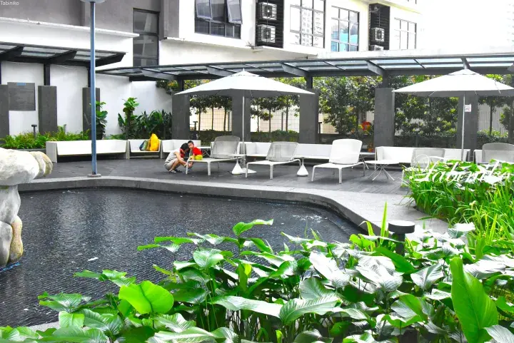 Modern hotel poolside lounge with white sun loungers, umbrellas, and lush greenery in a serene outdoor setting.