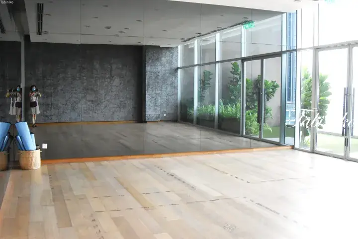 Spacious yoga studio with mirrored walls, wooden flooring, and large glass windows overlooking lush greenery.