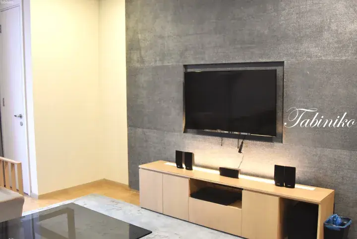 Modern living room with wall-mounted TV, wooden media console, and speakers against a textured grey accent wall.