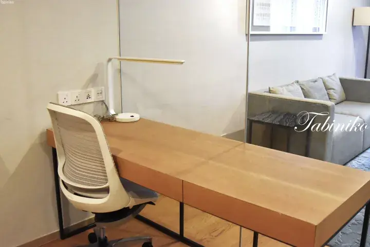 Modern wooden desk with mesh office chair and lamp in a bright room with sofa.