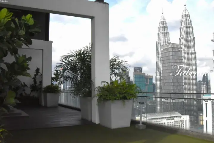 Modern balcony with lush greenery and glass railings overlooking the iconic Petronas Twin Towers in Kuala Lumpur.